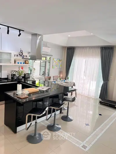 Modern kitchen with sleek black island and bar stools, open layout, and natural light from large windows.