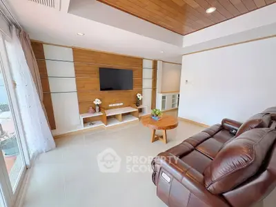 Modern living room with leather sofa and wooden accents, featuring a wall-mounted TV and natural light.