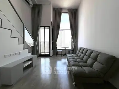 Modern living room with high ceiling and large windows offering city views, featuring a sleek sofa and minimalist decor.