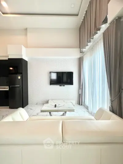Modern living room with white sofa, wall-mounted TV, and large windows with curtains.