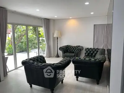 Spacious living room with elegant leather sofas and large windows overlooking lush greenery.