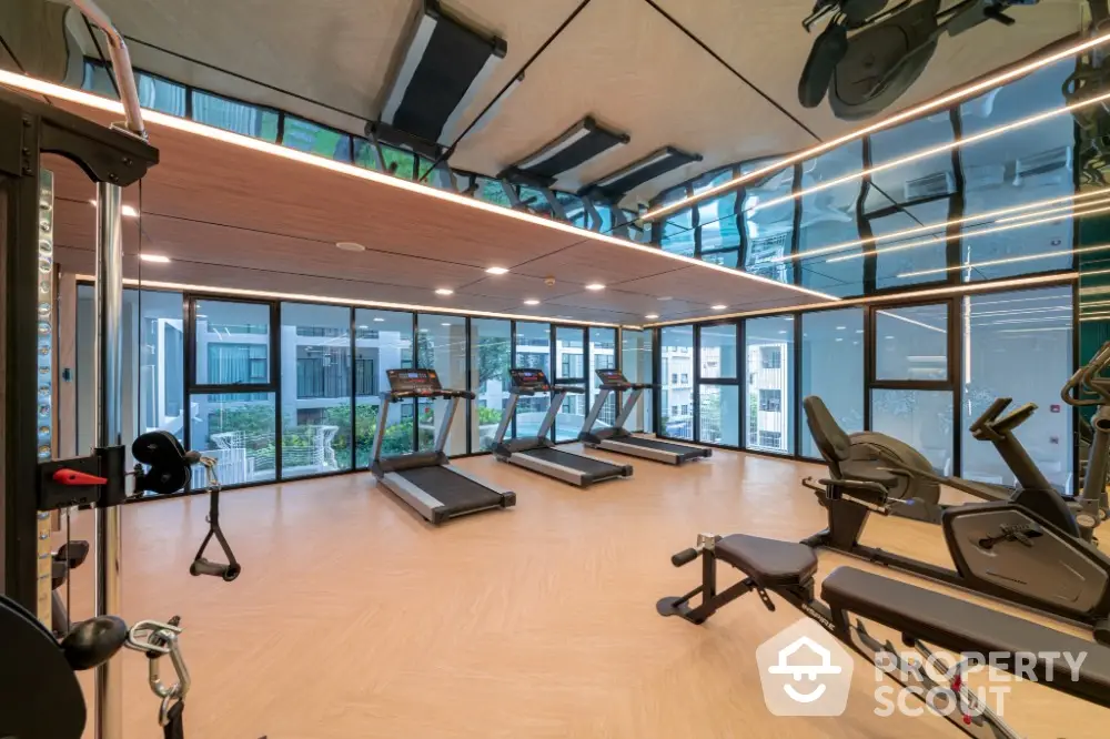 Modern gym with state-of-the-art equipment and floor-to-ceiling windows in luxury apartment complex.