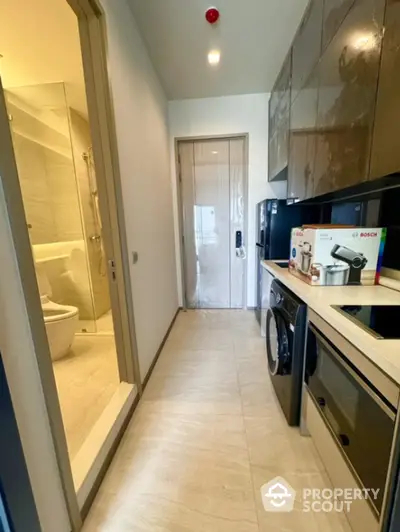 Modern kitchen with sleek appliances and adjacent bathroom in a contemporary apartment.