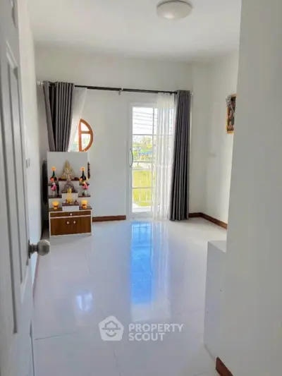Bright room with glossy white tiles and a small altar near a window with curtains.