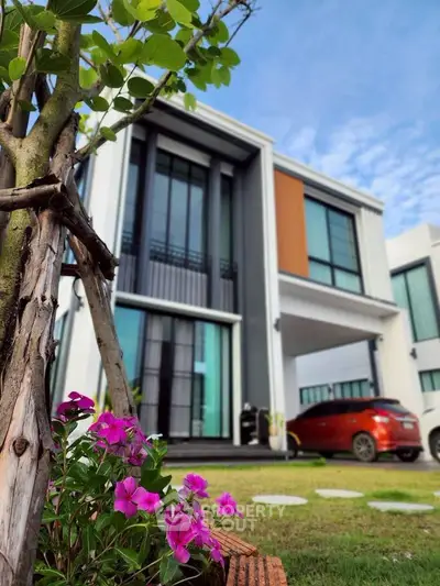 Modern two-story house with sleek design and vibrant garden, featuring a red car parked in the driveway.