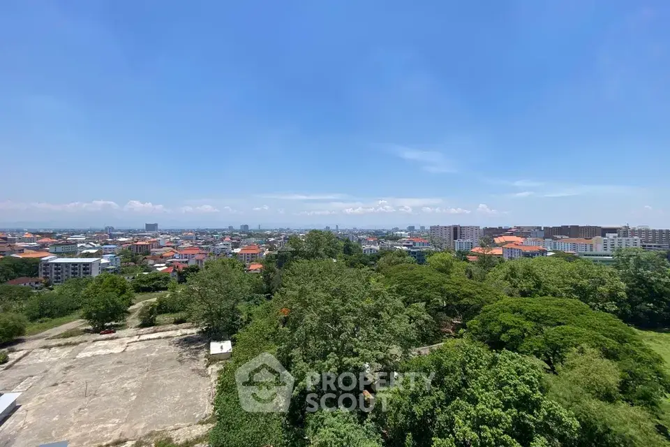 Stunning panoramic cityscape view from high-rise building, showcasing lush greenery and urban skyline under clear blue sky.