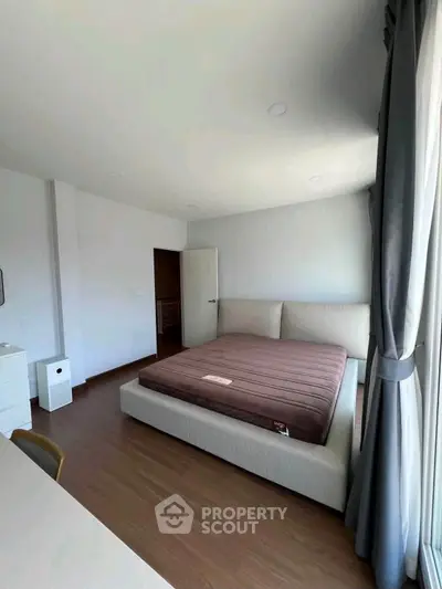 Spacious bedroom with large window and modern furnishings in a bright apartment.