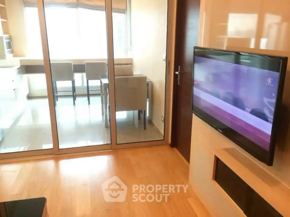 Modern living room with wall-mounted TV and glass partition to dining area.