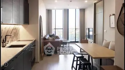 Modern living room with open kitchen, featuring sleek cabinetry and large windows with city view.