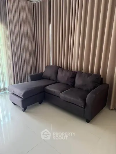 Elegant living room with modern dark sofa and floor-to-ceiling curtains, perfect for cozy relaxation.