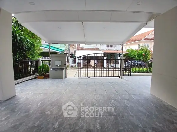 Spacious covered parking area with modern gate and tiled flooring in suburban home.