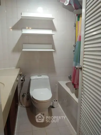 Compact bathroom with white tiles, toilet, and bathtub featuring colorful shower curtain.