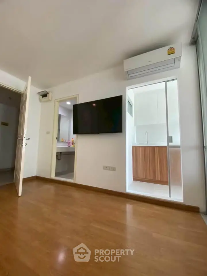 Modern apartment interior with wooden flooring, wall-mounted TV, and air conditioning unit.