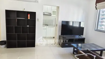 Modern living room with sleek black furniture and large TV, adjacent to a compact kitchen.