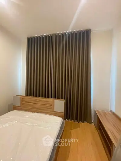 Cozy bedroom with wooden flooring and modern furnishings, featuring large windows with elegant curtains.