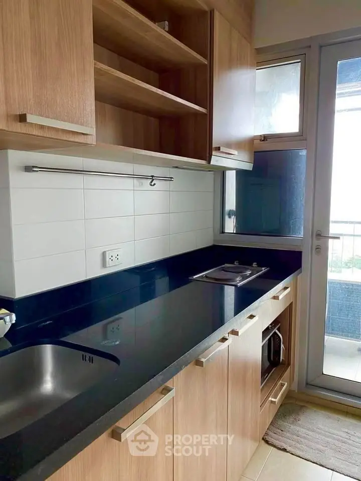 Modern kitchen with sleek black countertop and wooden cabinets, featuring a compact layout and natural light.
