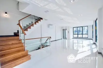 Spacious and modern living area with gleaming white floors, elegant wooden staircase, and abundant natural light from large windows, perfect for upscale urban living.