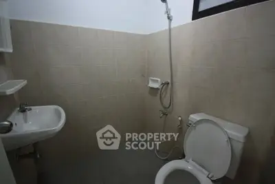 Compact bathroom with tiled walls, shower, toilet, and sink, ideal for small spaces.