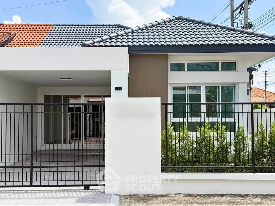 Charming single-story house with modern design and tiled roof, featuring a secure gated entrance and lush greenery.