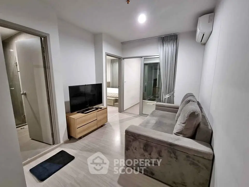 Modern living room with cozy sofa and flat-screen TV, adjacent to bedroom and bathroom.