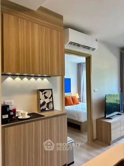 Modern apartment interior with compact kitchen and cozy bedroom view, featuring sleek wooden cabinetry and stylish decor.