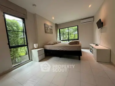 Spacious bedroom with large windows and modern decor, offering a serene garden view.