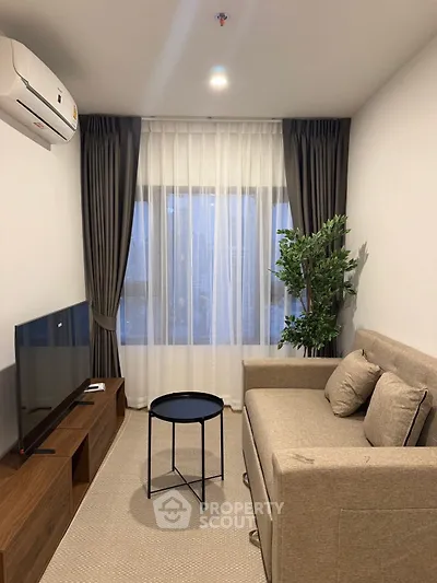 Cozy living room with modern sofa, TV, and large window with curtains.