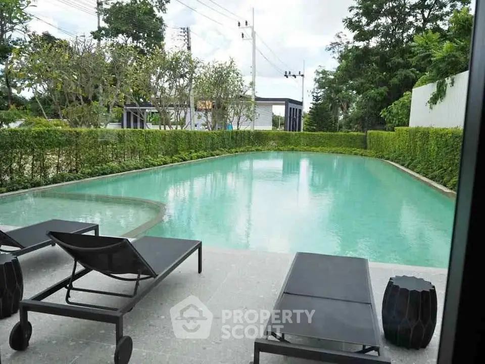 Luxurious outdoor pool area with modern lounge chairs and lush greenery, perfect for relaxation and leisure.