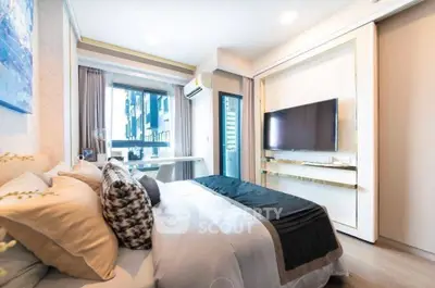 Modern bedroom with stylish decor and large TV, featuring a cozy bed and natural light from the window.