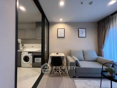 Modern living room with open kitchen and washing machine, featuring cozy sofa and dining area.