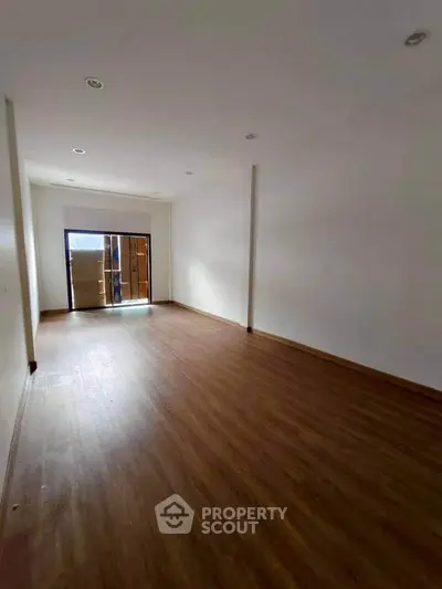Spacious empty room with wooden flooring and large window.