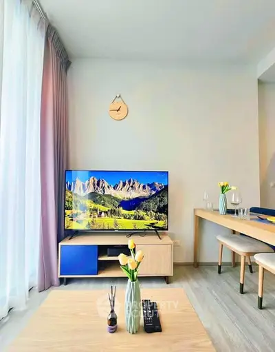 Modern living room with stylish decor and large TV, featuring natural light and elegant furnishings.