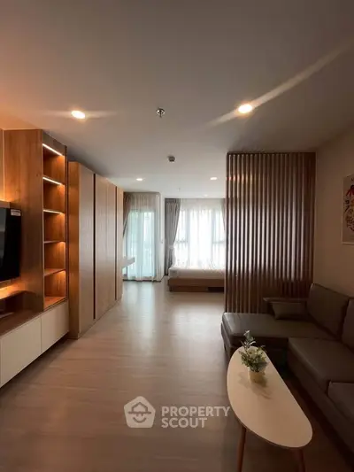 Modern open-plan living room with cozy seating and natural light, featuring elegant wooden accents and a view of the bedroom.