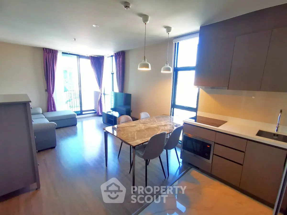 Modern open-layout living room with kitchen and dining area, featuring large windows and stylish furniture.