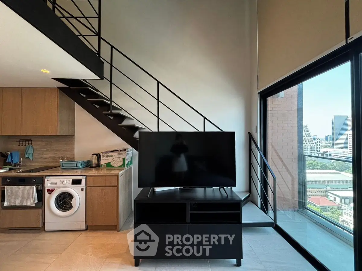 Modern loft apartment with open kitchen, washing machine, and city view from large window.