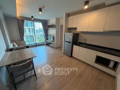 Modern open-plan living room with kitchen, featuring sleek cabinetry and large windows.