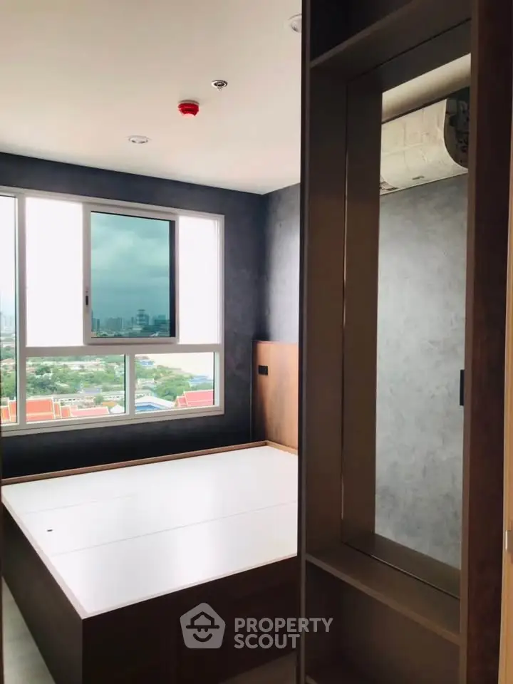 Modern bedroom with large window offering stunning city view, featuring sleek built-in storage solutions.