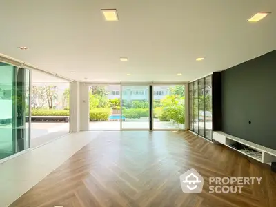 Spacious living room with herringbone wood flooring, floor-to-ceiling windows offering garden views, and modern lighting.