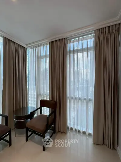 Spacious corner unit with large windows and elegant curtains, offering abundant natural light and a cozy seating area.