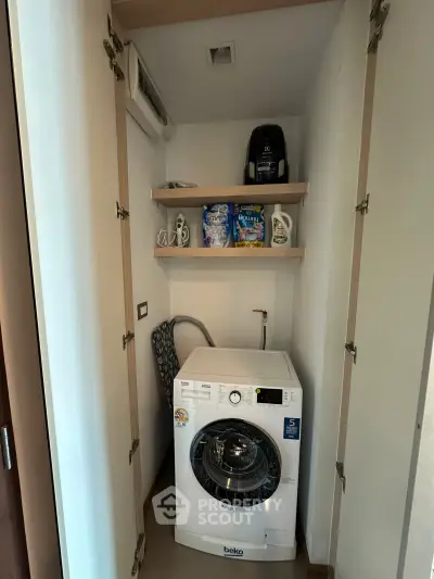 Compact laundry nook with washing machine and storage shelves in modern apartment.