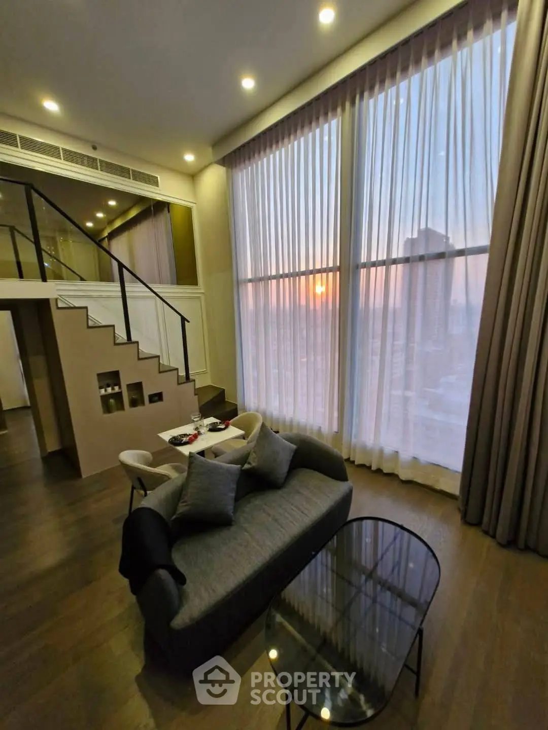 Luxurious high-ceiling living room with modern decor and stunning sunset view.