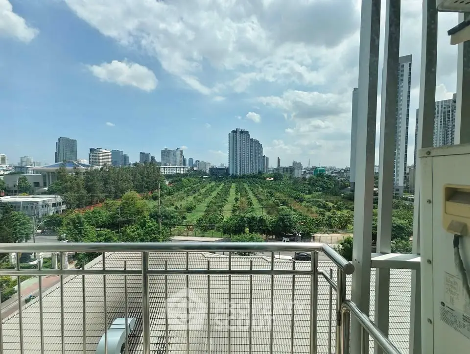 Stunning cityscape view from a balcony overlooking lush greenery and modern high-rise buildings.