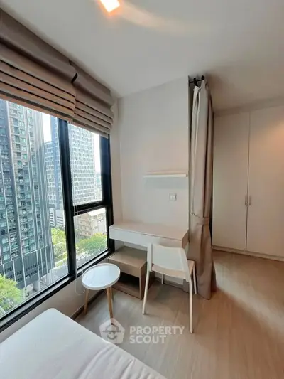 Modern bedroom with city view, featuring sleek furniture and large windows for natural light.