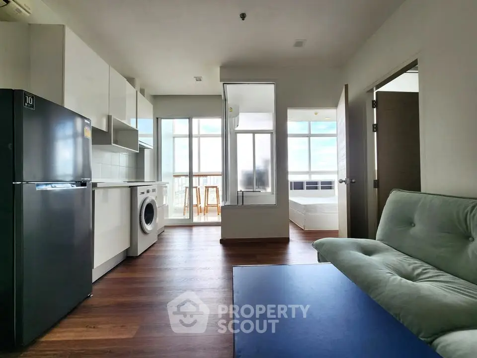 Modern apartment interior with open layout, featuring kitchen, living area, and bedroom with natural light.