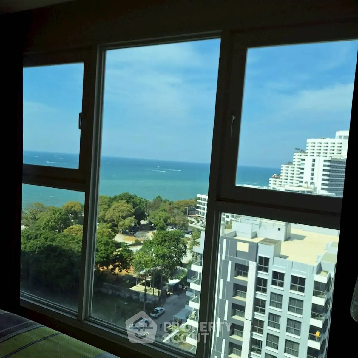 Stunning ocean view from high-rise apartment window, overlooking lush greenery and modern buildings.