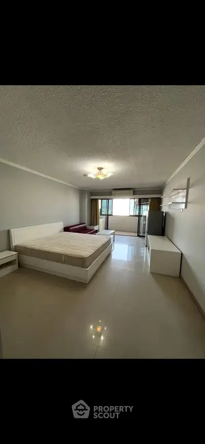Spacious bedroom with large windows and modern furnishings in a well-lit apartment.