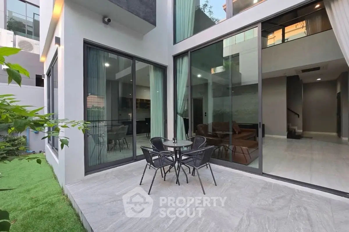 Modern home exterior with large glass doors and cozy patio seating area.