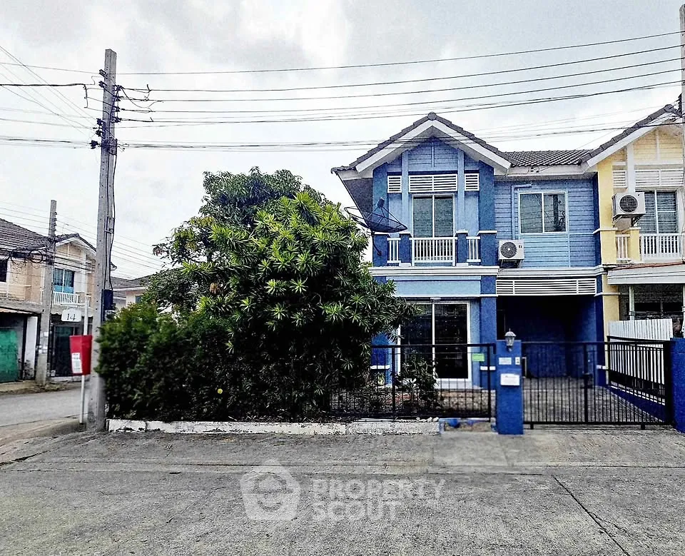 Charming blue two-story house with lush greenery and gated entrance in a serene neighborhood.