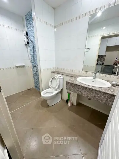 Modern bathroom with sleek design and spacious layout, featuring a large mirror and elegant tiles.