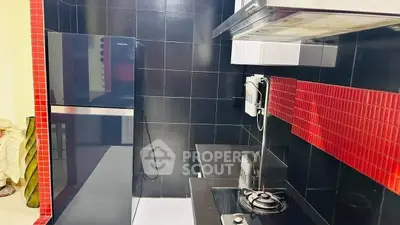 Modern kitchen with sleek black and red tile design, featuring a gas stove and refrigerator.
